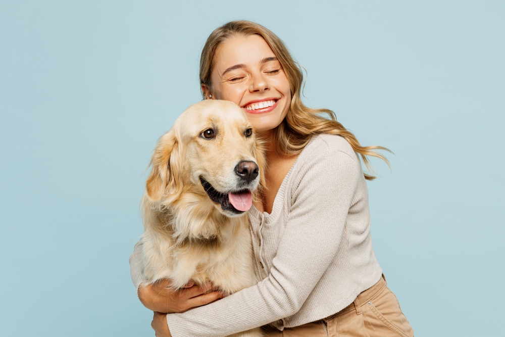 A cheerful woman embraces her happy Golden Retriever in front of a light blue background, expressing joy and relief following care from Emergency Vet St Augustine FL 